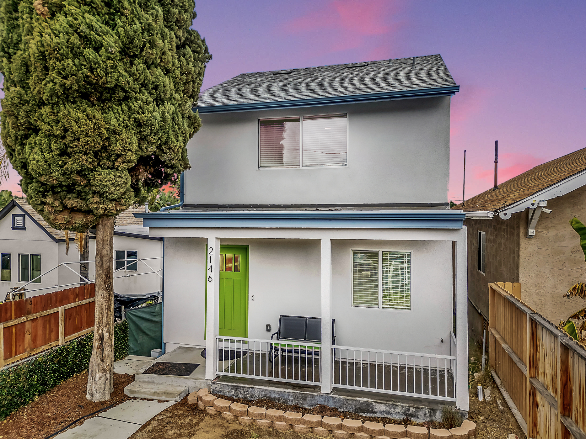 Front exterior view of 2146 Franklin Avenue in Logan Heights, featuring the heritage green front door and covered porch framed by a mature Cypress tree and fenced lot. Listed by Portia Green, REALTOR® at Compass in San Diego.