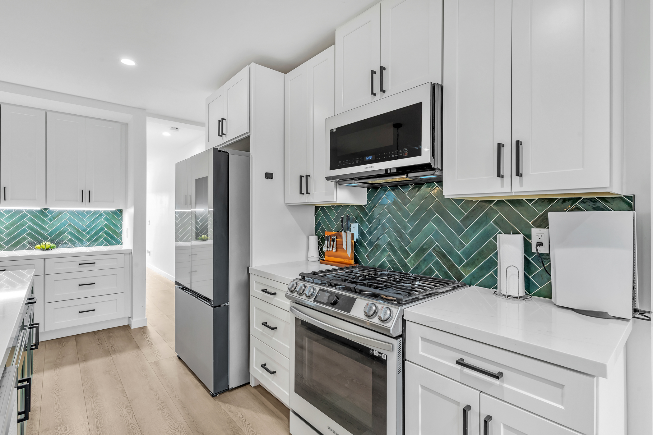 Bright, modern kitchen at 2145 Franklin Avenue in Logan Heights featuring white shaker cabinets, stainless steel Samsung appliances, and a green herringbone tile backsplash with under-cabinet lighting. Listed by Portia Green, REALTOR® at Compass in San Diego.