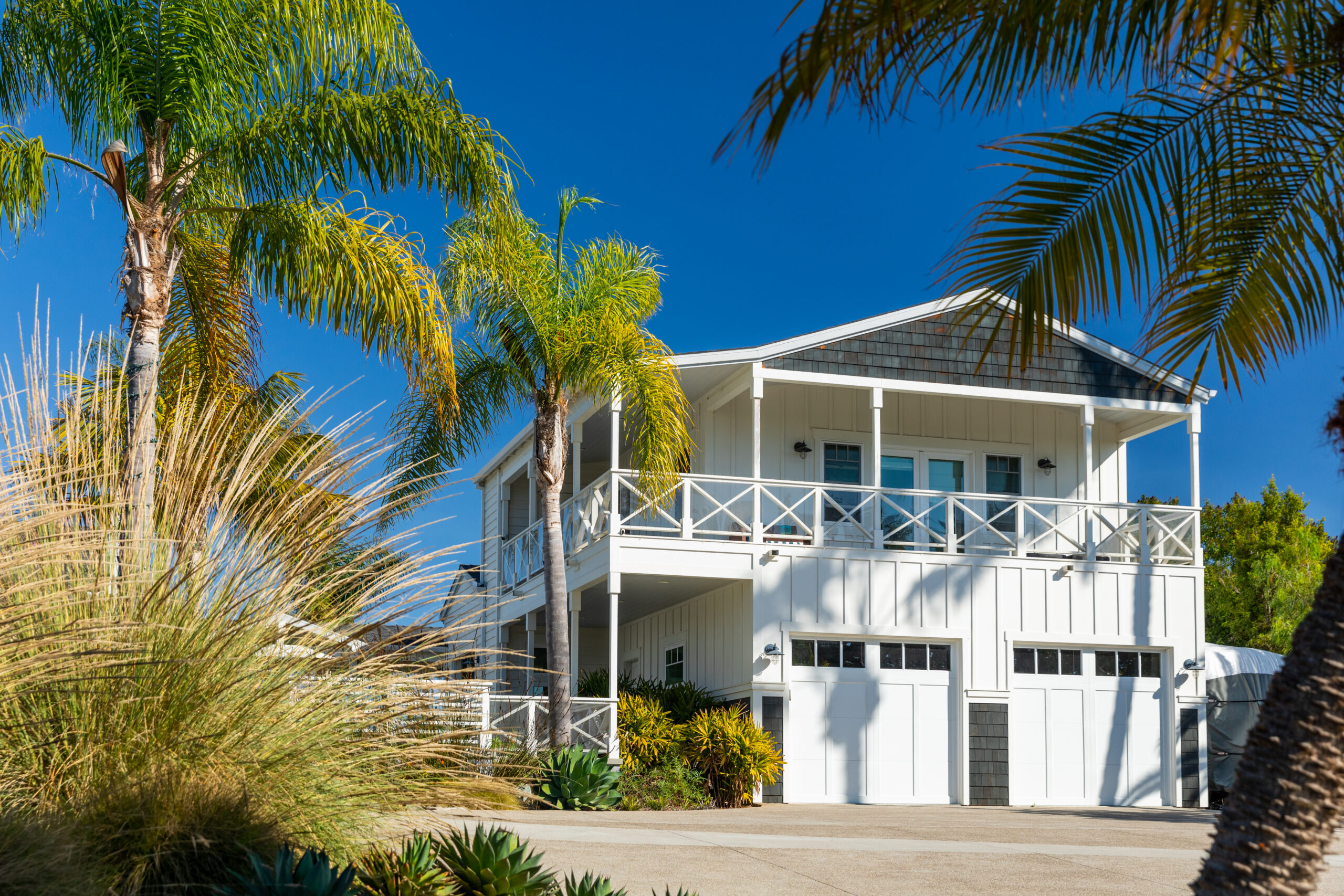 Modern farmhouse-style home in Carlsbad with white siding, wood accents, and palm trees